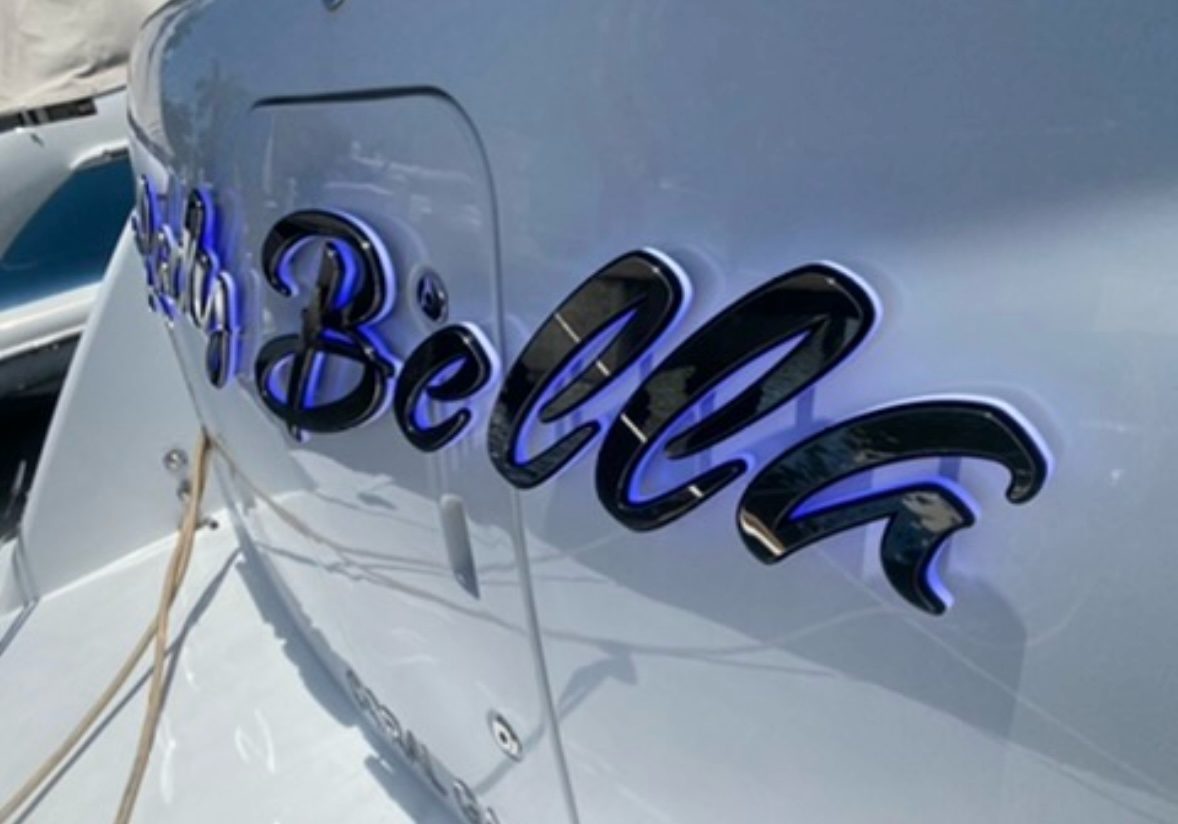 Bella in glossy black script letters with blue halo on a white hull