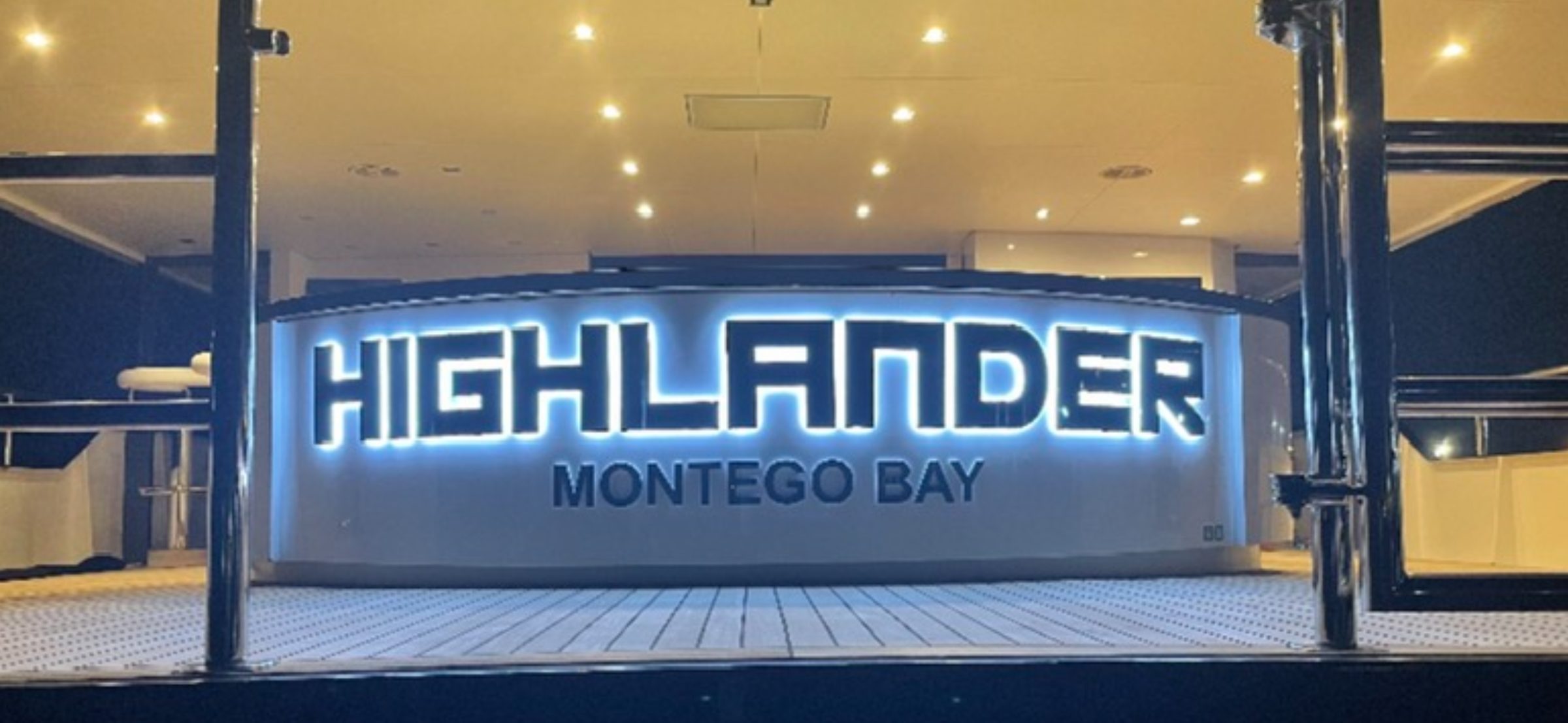 HIGHLANDER with MONTEGO BAY home port, black-faced letters with white halo on a curved aft bulkhead at night