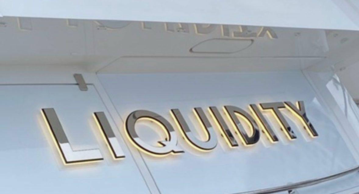 LIQUIDITY mirror-polished letters with warm halo glow on a white transom
