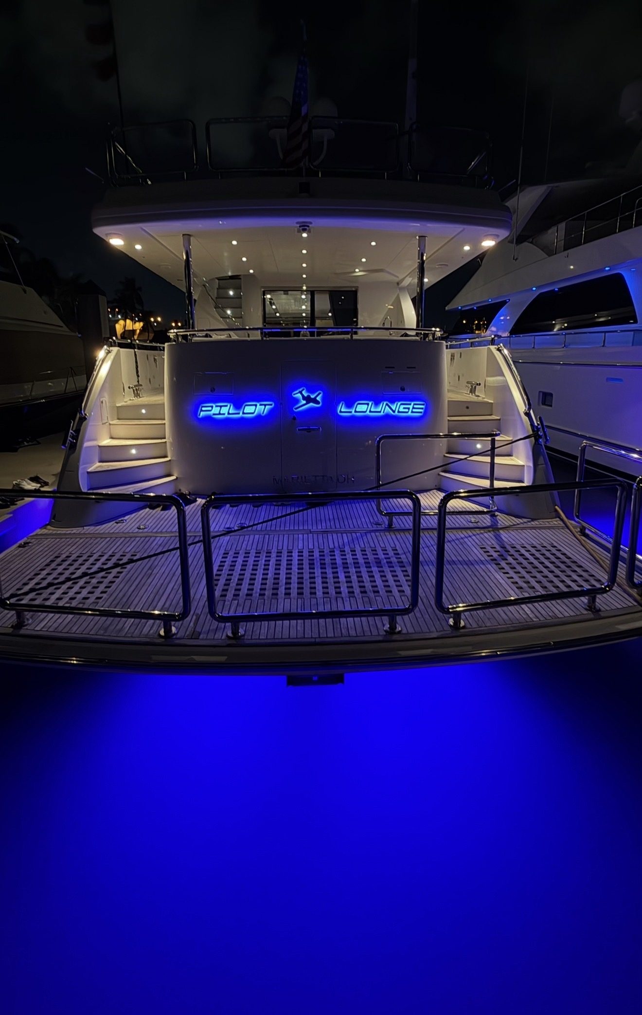 PILOT LOUNGE in blue-lit letters with a custom airplane logo on a yacht's aft deck at night