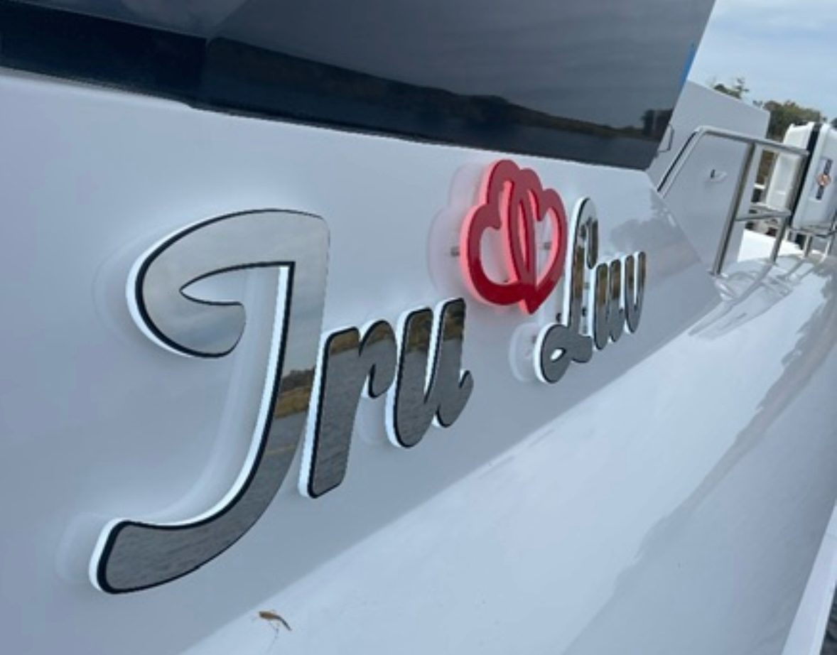 Tru Luv in polished stainless script with a red-lit heart logo, daylight