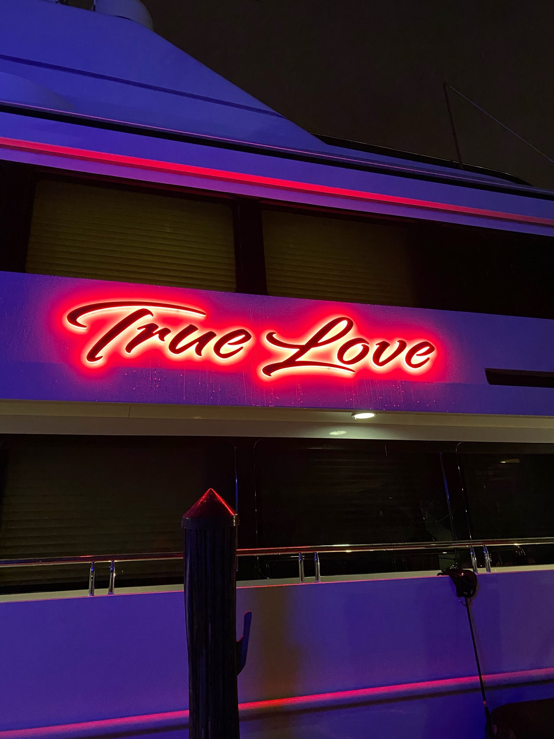 True Love in red-lit script letters on a yacht's hull side at night